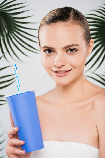 happy woman holding disposable cup with straw near palm leaves on white  - Photo, Image