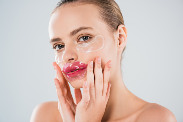 attractive woman with lip mask and eye patches touching clean face isolated on grey - Φωτογραφία, εικόνα