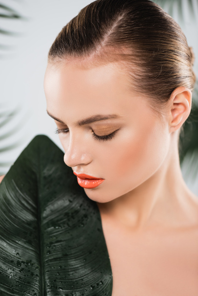 attractive woman with makeup looking at green leaf on white  - Foto, afbeelding