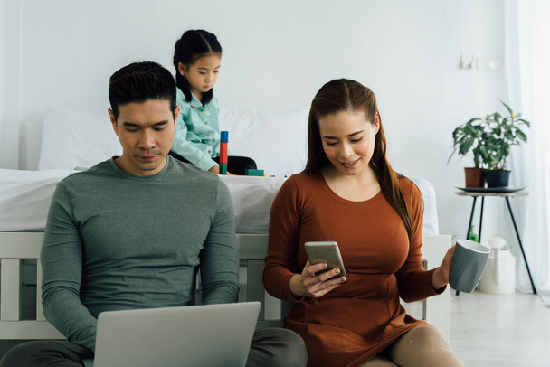 Couple using laptop and phone with daughter in background - Foto, afbeelding