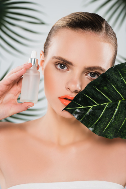 attractive woman holding bottle with serum near leaf on white - Foto, Imagem