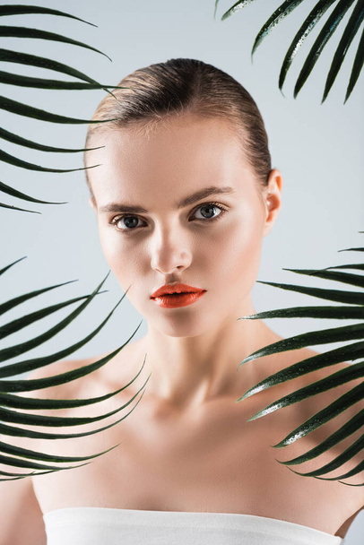 pretty woman with makeup looking at camera near palm leaves on white  - Фото, зображення