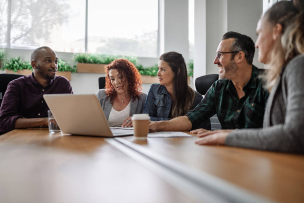 Equipe diversa de empresários sorridentes que têm uma reunião em torno de uma mesa de conferência em um escritório - Foto, Imagem