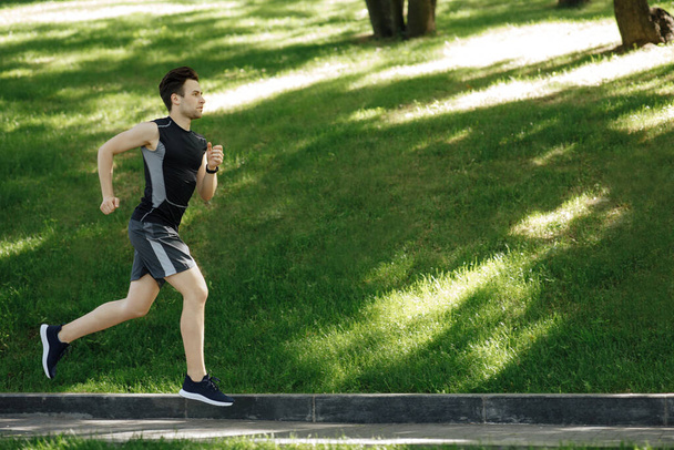 Un sportif dans le parc. Le gars en vêtements de sport avec des baskets et un tracker de fitness court sur la piste - Photo, image