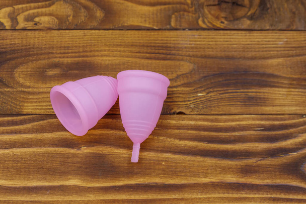 Różowe silikonowe kubki menstruacyjne wielokrotnego użytku na drewnianym tle. Widok góry. Pojęcie higieny kobiecej, ginekologii i zdrowia - Zdjęcie, obraz