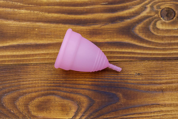 Růžové opakovaně použitelný silikonový menstruační šálek na dřevěném pozadí. Horní pohled. Koncepce ženské hygieny, gynekologie a zdraví - Fotografie, Obrázek