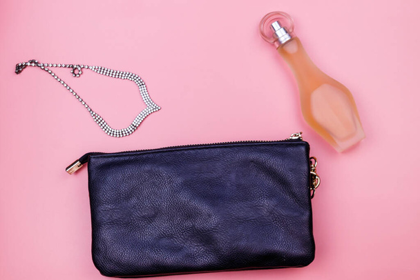 Koppelingszak, ketting en flesje parfum op roze achtergrond. Bovenaanzicht. Schoonheids- en modeconcept - Foto, afbeelding
