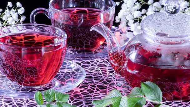 Hibiscus Rode thee mok met anjer bloemen close-up horizontale foto.Engelse thee traditie.Medicinale therapie op basis van geneeskrachtige kruiden en afleidingen.Kruidige kruiden en medicinale borstels.Een ontspannen drankje - Foto, afbeelding