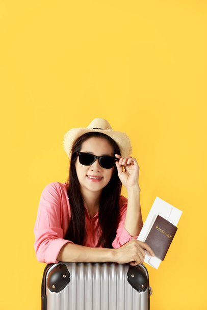 Азійські жінки носять солом'яний капелюх, сонцезахисні окуляри в руці тримають паспортну книжку і пакет подорожей з копіювальним прапором. Дівчинка готова подорожувати з валізою і паспортом на жовтому тлі. Літо - Фото, зображення