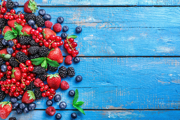 Куча разнообразных свежих ягод на синем деревянном фоне. Вид сверху. Копирование пространства. - Фото, изображение