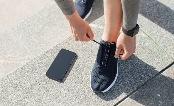 Healthy lifestyle, sport and exercise. Guy with fitness tracker tie laces on sneakers, telephone on floor near - Fotografie, Obrázek