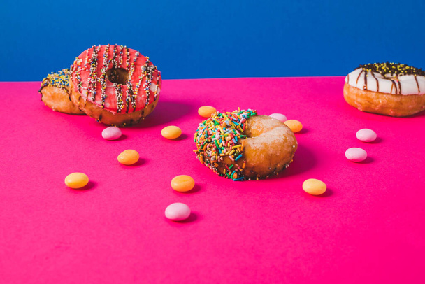 ピンクのアンブブルーの背景にキャンディでカラフルなドーナツ - 写真・画像