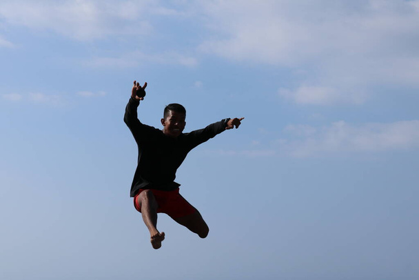 Šťastný han skákání nad modrou oblohou pozadí. Mladé veselé indonéské skoky. Mladík v dobré náladě vyskočí do vzduchu. Slunečný tropický den. - Fotografie, Obrázek
