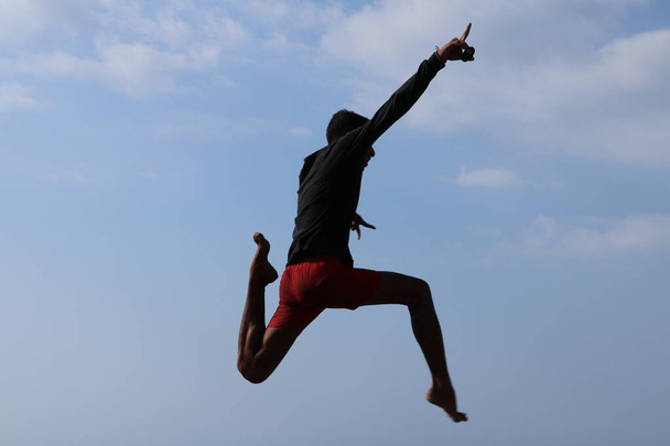 Щасливий Хан стрибає над синім небом. Веселі індонезійські стрибки. Підліток у доброму настрої стрибає в повітря. Сонячний тропічний день. - Фото, зображення