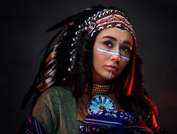 Portrait of a beautiful American Indian woman in ethnical costume and traditional make up - Фото, зображення