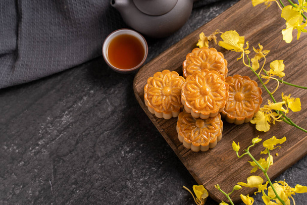 Mooncake, Moon cake for Mid-Autumn Festival, concept of traditional festive food on black slate table with tea and yellow flower, close up, copy space. - 写真・画像