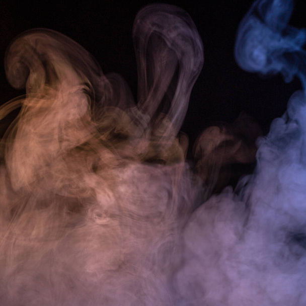 Conceptual image of multi-colored smoke isolated on dark black background and wooden table. - Foto, afbeelding