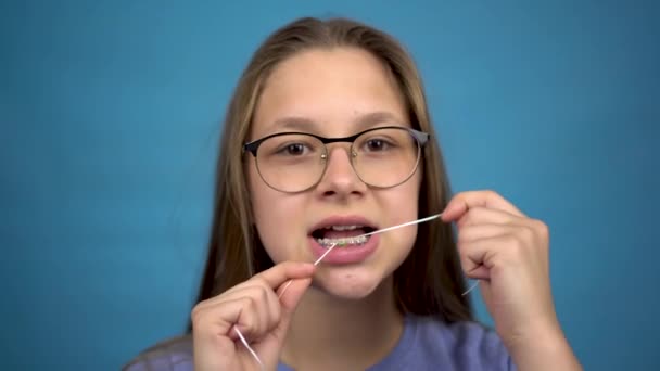 歯をデンタルフロスでブラッシングしている女の子。彼女の歯に色のブレースを持つ女の子は彼女の歯をきれいに保つ. - 映像、動画