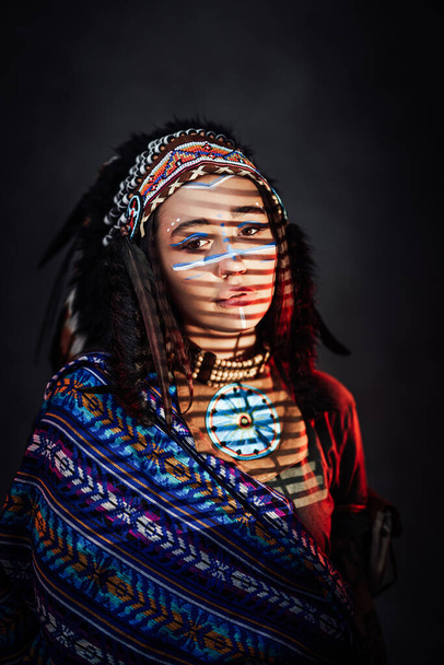 Kaunis amerikkalainen intialainen tyttö, jolla on perinteinen meikki intialaisessa höyhenhatussa ja etnisissä vaatteissa - Valokuva, kuva