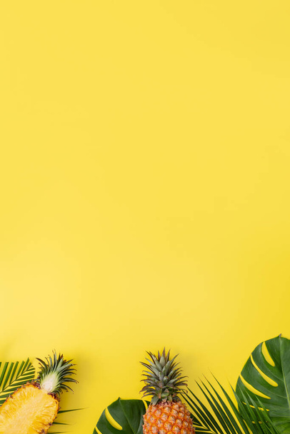 Beautiful pineapple on tropical palm monstera leaves isolated on bright pastel yellow background, top view, flat lay, overhead above summer fruit. - 写真・画像