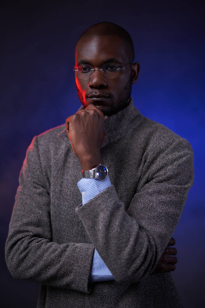 Uomo afroamericano di successo in giacca grigia e occhiali, tiene la mano sul mento - Foto, immagini