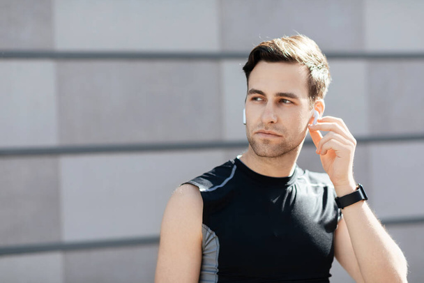 Music for jogging outside. Serious guy in sportswear puts wireless headphones - Photo, Image
