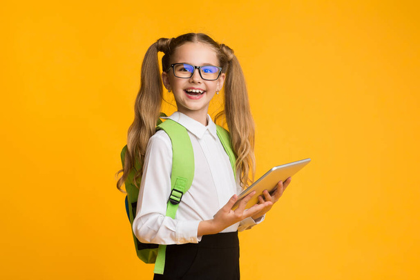 Feliz colegiala sosteniendo tableta digital posando sobre fondo de estudio amarillo
 - Foto, Imagen