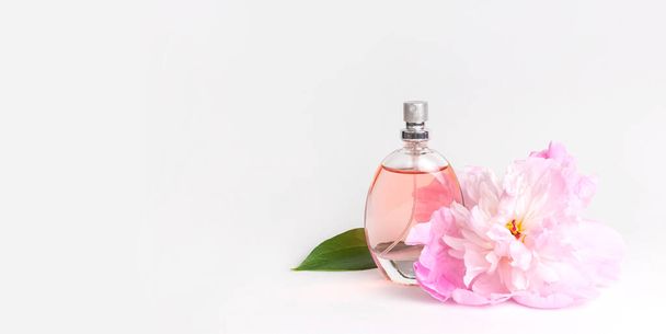 Beautiful composition with perfume and flowers. Perfume bottle, pink flowers peonies green leaves on light background Flat lay copy space Perfumery cosmetics toilet water fragrance collection. - Foto, Imagem
