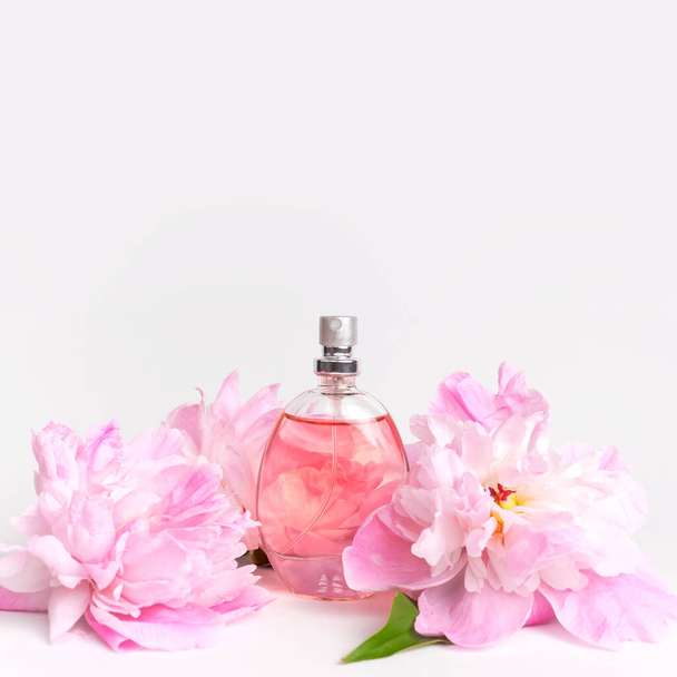 Όμορφη σύνθεση με άρωμα και λουλούδια. Μπουκαλάκι αρωμάτων, ροζ λουλούδια παιώνιες πράσινα φύλλα σε ανοιχτό φόντο Επίπεδος χώρος αντιγραφής Αρωματικά καλλυντικά προϊόντα περιποίησης συλλογή αρωμάτων νερού τουαλέτας. - Φωτογραφία, εικόνα
