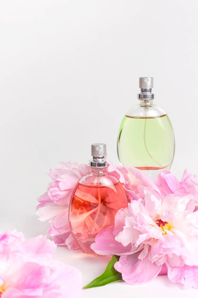 Beautiful composition with perfume and flowers. Perfume bottle, pink flowers peonies green leaves on light background Flat lay copy space Perfumery cosmetics toilet water fragrance collection. - Photo, Image