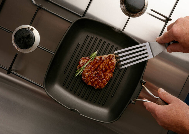 Hagyományos gormet steaket sütök rozmaringgal, és lapos térrel egy rozsdamentes gáztűzhelyen. - Fotó, kép