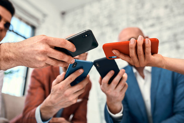 Male and female diverse hands holding cell phones, multiracial business people using smartphones applications software, users and devices concept, mobile communication - Photo, Image