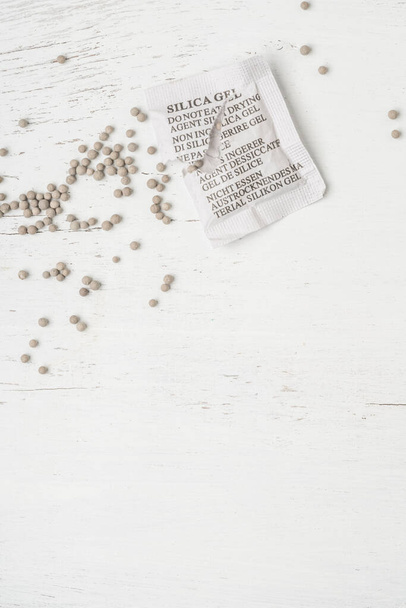 Desiccant or silica gel in white paper packaging, spread on the wooden background with copy space - Photo, Image