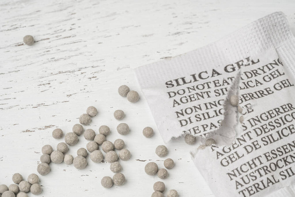 Desiccant or silica gel in white paper packaging, spread on the wooden background - Photo, Image