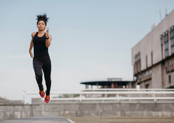 Correr, saltar y volar. Atlético delgado afroamericano chica en uniforme deportivo de moda congelado en el aire
 - Foto, imagen