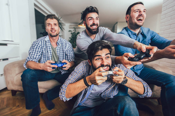 Sorrindo amigos do sexo masculino jogando videogames em casa e se divertindo
. - Foto, Imagem