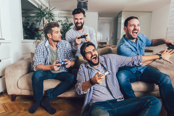 笑顔の男性の友人は自宅でビデオゲームをプレイし、楽しみを持って. - 写真・画像
