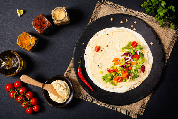 Tortilla with vegetables and hummus with chickpeas. Top view. Black background.  - Zdjęcie, obraz