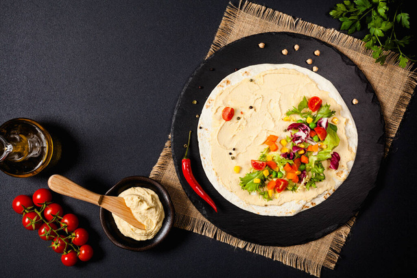Tortilla with vegetables and hummus with chickpeas. Top view. Black background.  - Photo, Image