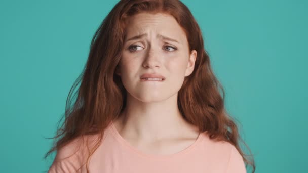 Beautiful worried redhead girl shyly looking in camera and smiling over colorful background. Face expression - Footage, Video