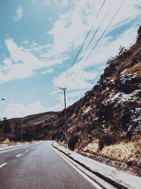 Dry asphalt empty automobile road with marking lines near rocks on a sunny summer day with blue cloudy sky. Car travel trip concept background. Stories vertical format. Dark green style - 写真・画像