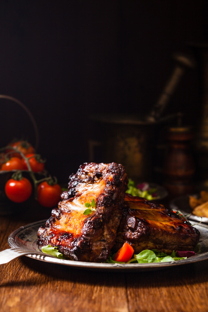 Roasted ribs, served on an old plate. Fron view. Dark or balck background. - Fotó, kép