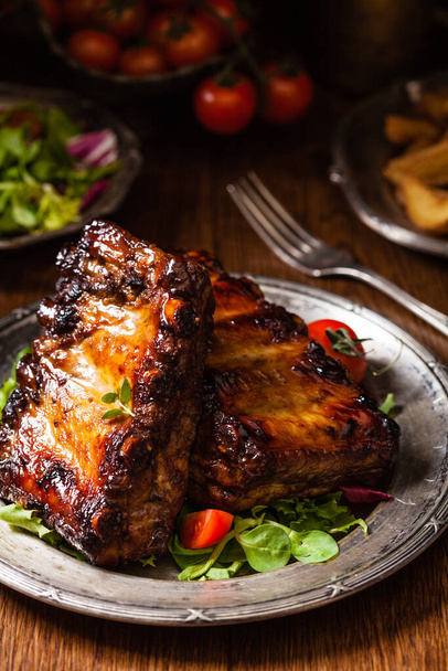 Roasted ribs, served on an old plate. Fron view. Dark or balck background. - Foto, Bild