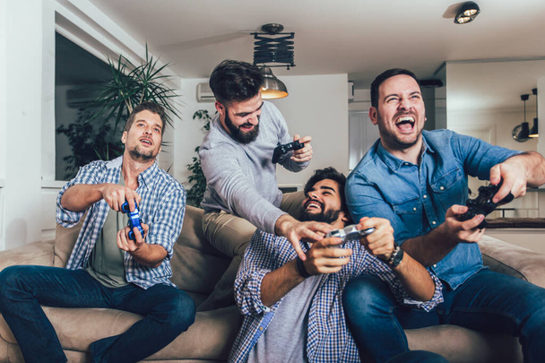 Uśmiechnięci przyjaciele grający w gry wideo w domu i bawiący się. - Zdjęcie, obraz