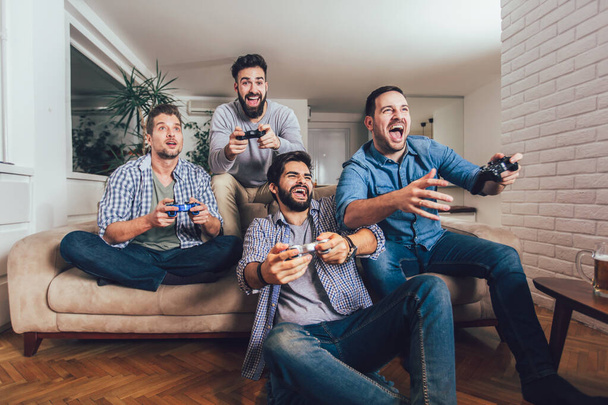 Lachende mannelijke vrienden spelen videospelletjes thuis en hebben plezier. - Foto, afbeelding