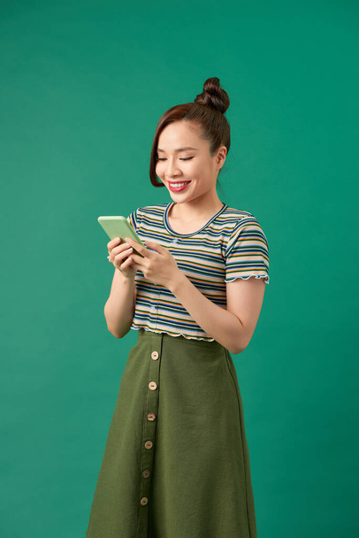Portrait of a smiling casual woman holding smartphone over green background - Photo, Image