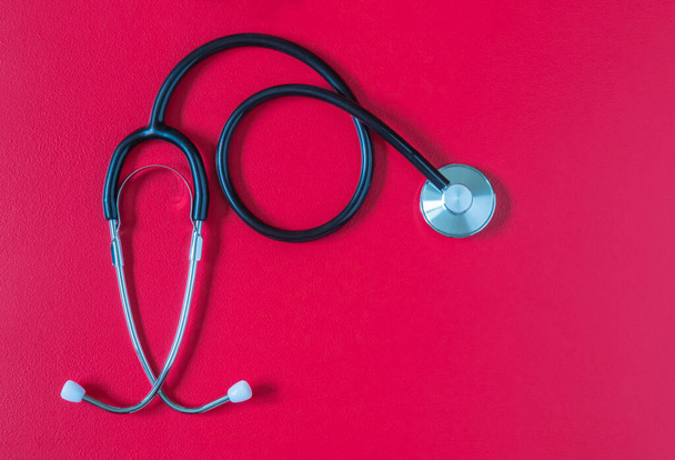 Medical stethoscope on red background with copy space. Flat lay isolated of stethoscope on red backdrop. Mockup for medical and health care. Healthcare and cardiology concept - Photo, Image
