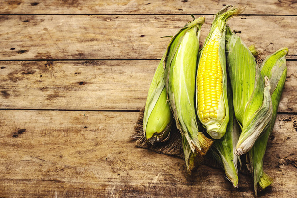Fresh corn cobs in peel. New harvest, on sackcloth, wooden boards background, copy space - Photo, Image