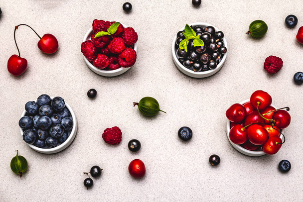Assorted berries in bowls: bilberry, blueberry, currant, blackberry, cherry and raspberry. Stone concrete background, top view - Foto, Imagem