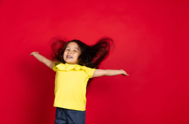 Beautiful emotional little girl isolated on red background. Half-lenght portrait of happy child gesturing - Фото, изображение